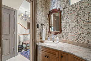 Bathroom with wallpapered walls, a chandelier, and vanity