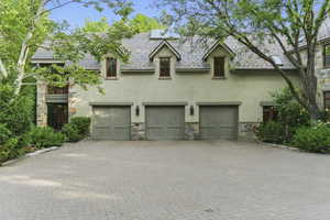View of front of home with stucco siding, stone siding, a garage, decorative driveway, and a high end roof