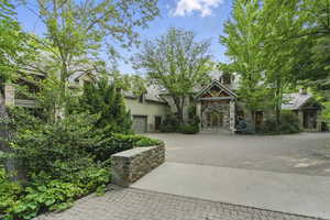 View of front facade with stone siding, decorative driveway, an attached garage, stucco siding, and french doors