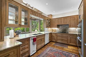 Kitchen with dishwasher, plenty of natural light, light stone counters, brown cabinets, and recessed lighting