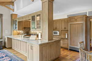 Kitchen featuring light wood-style floors, white microwave, light stone countertops, a peninsula, and backsplash