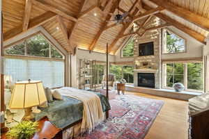 Bedroom with high vaulted ceiling, a wood ceiling with exposed beams, wood finished floors, a tile fireplace, and multiple windows