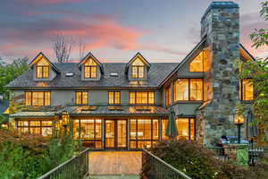 Back of house at dusk featuring a standing seam roof, stucco siding, a metal roof, a chimney, and a high end roof