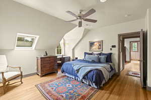 Bedroom featuring wood finished floors, multiple windows, ceiling fan, and vaulted ceiling