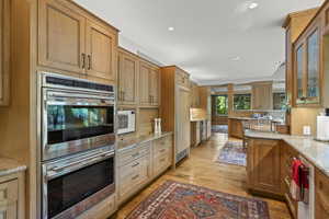 Kitchen with double oven, light wood-type flooring, light stone countertops, recessed lighting, and white microwave