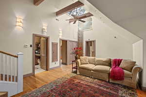 Living room featuring high vaulted ceiling, light wood-style floors, ceiling fan, beamed ceiling, and stairs