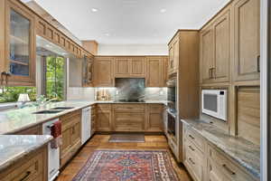 Kitchen featuring white appliances, wood finished floors, light stone countertops, tasteful backsplash, and glass insert cabinets