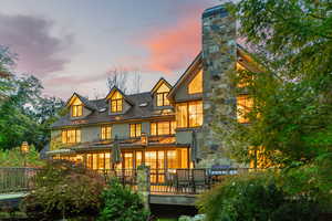 Back of property at dusk with a standing seam roof, stucco siding, a chimney, a metal roof, and a wooden deck
