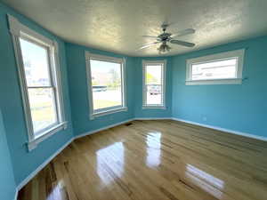 Unfurnished room with a textured ceiling, wood finished floors, plenty of natural light, and ceiling fan