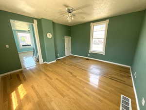 Empty room with ceiling fan, a textured ceiling, and wood finished floors