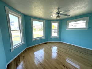 Spare room featuring a textured ceiling, healthy amount of natural light, wood finished floors, and ceiling fan