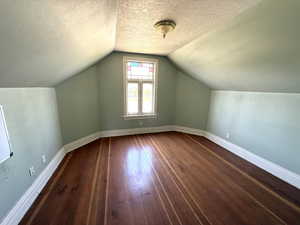 Additional living space with dark wood-style floors, a textured ceiling, and lofted ceiling