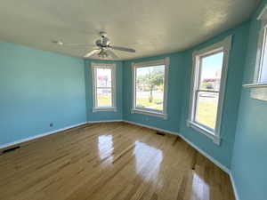 Unfurnished room with wood finished floors, a textured ceiling, healthy amount of natural light, and a ceiling fan