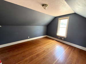 Bonus room featuring hardwood / wood-style flooring, a textured ceiling, and vaulted ceiling