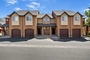 View of property featuring a garage, stone siding, and stucco siding