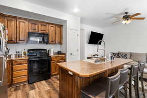 Kitchen featuring black appliances, ceiling fan, a breakfast bar area, and dark wood finished floors