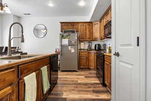 Kitchen featuring black appliances, wood finished floors, recessed lighting, brown cabinets, and a textured ceiling