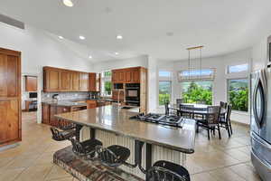 Kitchen featuring appliances with stainless steel finishes, recessed lighting, brown cabinetry, a center island with sink, and a breakfast bar