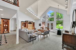 Carpeted living area with high vaulted ceiling, arched walkways, and a chandelier