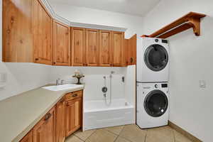 Laundry room featuring stacked washer and dryer, cabinet space, and light tile patterned flooring, and dog washing tub with sprayer
