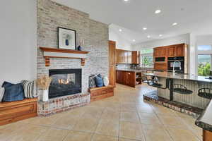Kitchen with vaulted ceiling, light tile patterned flooring, black appliances, recessed lighting, and a kitchen bar, gas fireplace