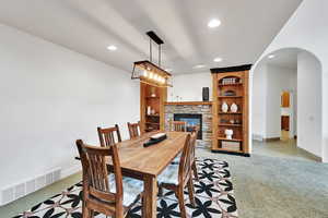 Dining room with light colored carpet, arched walkways, recessed lighting, and a stone fireplace
