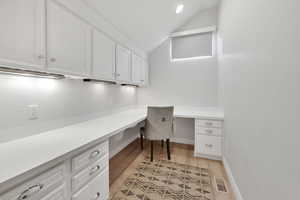 ADU office space with built in desk, lofted ceiling, and light wood-style floors, remote blinds