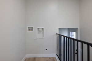 Laundry room with hookup for a washing machine, electric dryer hookup, light wood-style floors, and a high ceiling
