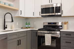 Kitchen featuring stainless steel appliances, gray cabinetry, light countertops, backsplash, and open shelves