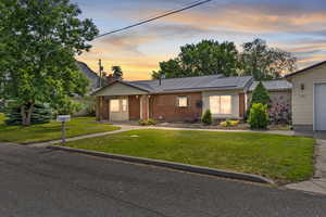 View of front facade with brick siding, a front yard, a chimney, and a metal roof