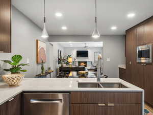 Kitchen with stainless steel appliances, a warm lit fireplace, decorative light fixtures, recessed lighting, and modern cabinets