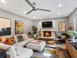 Living room with wood finished floors, a fireplace, ceiling fan, and recessed lighting