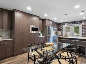 Kitchen featuring appliances with stainless steel finishes, light wood finished floors, hanging light fixtures, light countertops, and dark brown cabinets