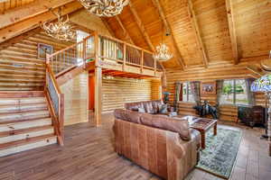 Living area featuring a chandelier, a wood stove, stairs, a wood ceiling with exposed beams, and log walls