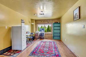 Office area with a textured ceiling, light wood-type flooring, a chandelier, and log walls