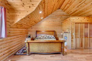 Bedroom featuring log walls, vaulted ceiling, wood ceiling, and wood finished floors