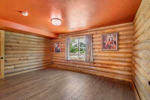 Empty room featuring a textured ceiling, wood finished floors, log walls, and a smoke detector