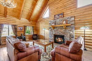 Living area featuring rustic walls, high vaulted ceiling, a wood ceiling with exposed beams, a stone fireplace, and a chandelier