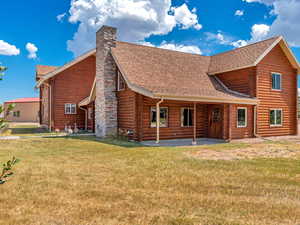 Rear view of house with roof with shingles, a patio area, a yard, a chimney, and log siding