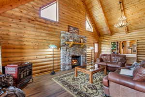 Living area featuring high vaulted ceiling, a wood stove, a chandelier, log walls, and a fireplace