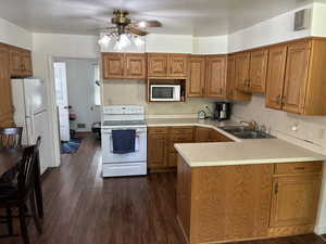 Kitchen with white appliances, brown cabinetry, light countertops, ceiling fan, and a peninsula