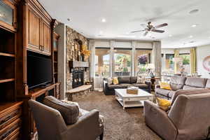 Living room with a stone fireplace, dark carpet, recessed lighting, and a ceiling fan
