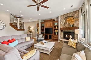 Carpeted living room with a ceiling fan, stairway, recessed lighting, and a stone fireplace