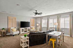 Carpeted living room with ceiling fan and a textured ceiling