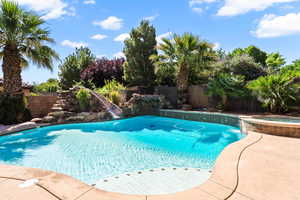 View of swimming pool with a water slide, a fenced backyard, and a pool with connected hot tub