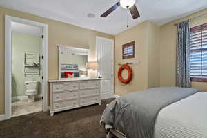Bedroom with ensuite bath, dark colored carpet, and a ceiling fan