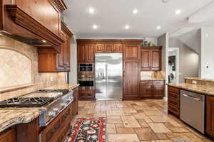 Kitchen with stainless steel appliances, washer / dryer, custom range hood, recessed lighting, and stone tile floors