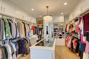 Spacious closet with arched walkways, light wood finished floors, and a chandelier