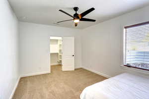 Bedroom featuring light colored carpet, a spacious closet, a ceiling fan, and a closet