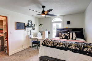 Bedroom featuring carpet, a spacious closet, a textured ceiling, and ceiling fan
